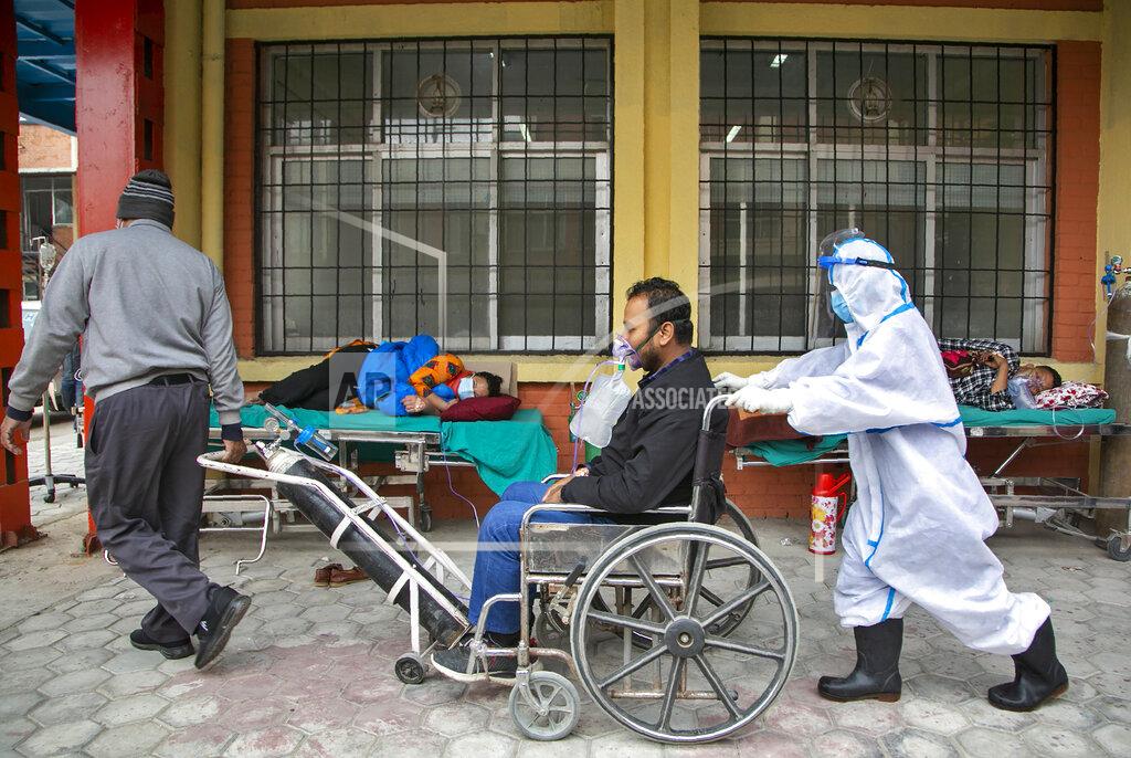 Niranjan Shrestha A COVID-19 patient arrives on a wheelchair as others are lying down on beds outside an emergency ward of a government run hospital in Kathmandu, Nepal, Friday, May 7, 2021. Across the border from a devastating surge in India, doctors in Nepal warned Friday of a major crisis as daily coronavirus cases hit a record and hospitals were running out of beds and oxygen. (AP Photo/Niranjan Shrestha)
