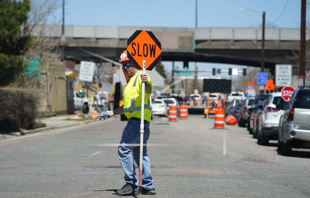 David Zalubowski In this Thursday, April 29, 2021, photograph, a traffic worker advises motorists headed northbound along York Street as construction continues on what will become Interstate 70 north of downtown Denver. The elevated roadway that has served as Interstate 70 will be demolished as part of the 10-mile-long project, which will cost $1.2 billion by completion by winter 2022. (AP Photo/David Zalubowski)