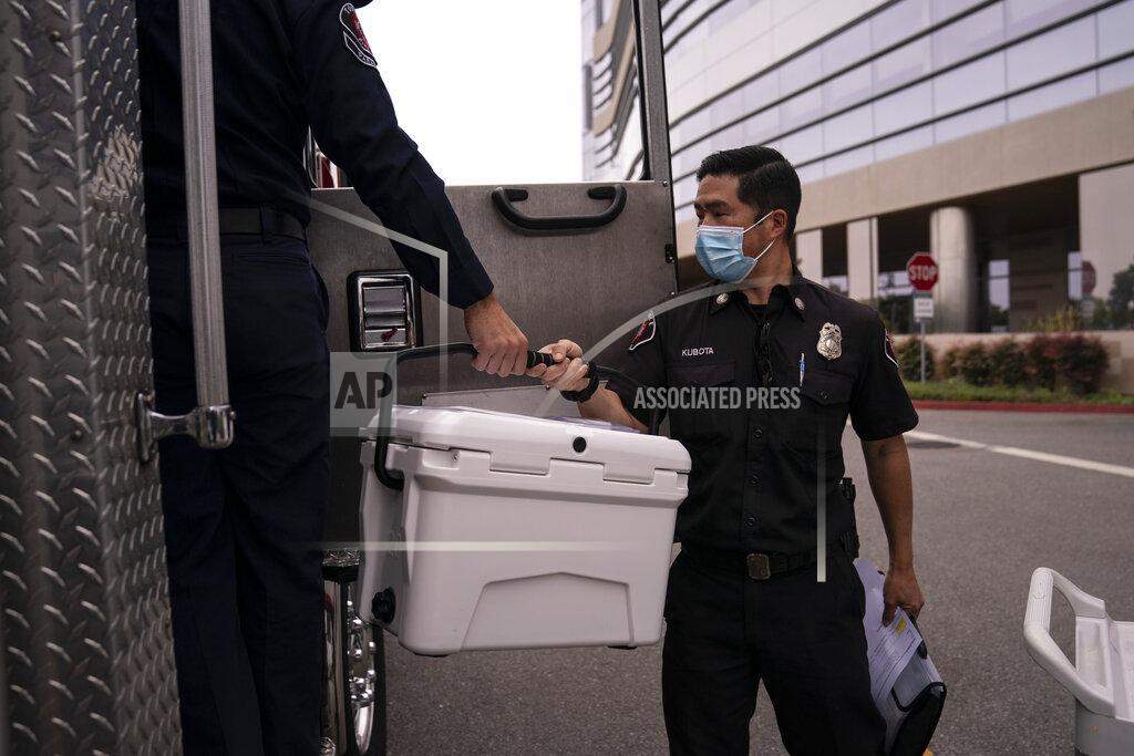 Jae C. Hong Torrance fire Capt. John Kubota, right, hands a cooler containing the Pfizer COVID-19 vaccine to Alessandro Demuro as they prepare to inoculate two sisters who have muscular dystrophy, at their home, Wednesday, May 12, 2021, in Torrance, Calif. Teamed up with the Torrance Fire Department, Torrance Memorial Medical Center started inoculating people at home in March, identifying people through a city hotline, county health department, senior centers and doctor's offices, said Mei Tsai, the pharmacist who coordinates the program. (AP Photo/Jae C. Hong)