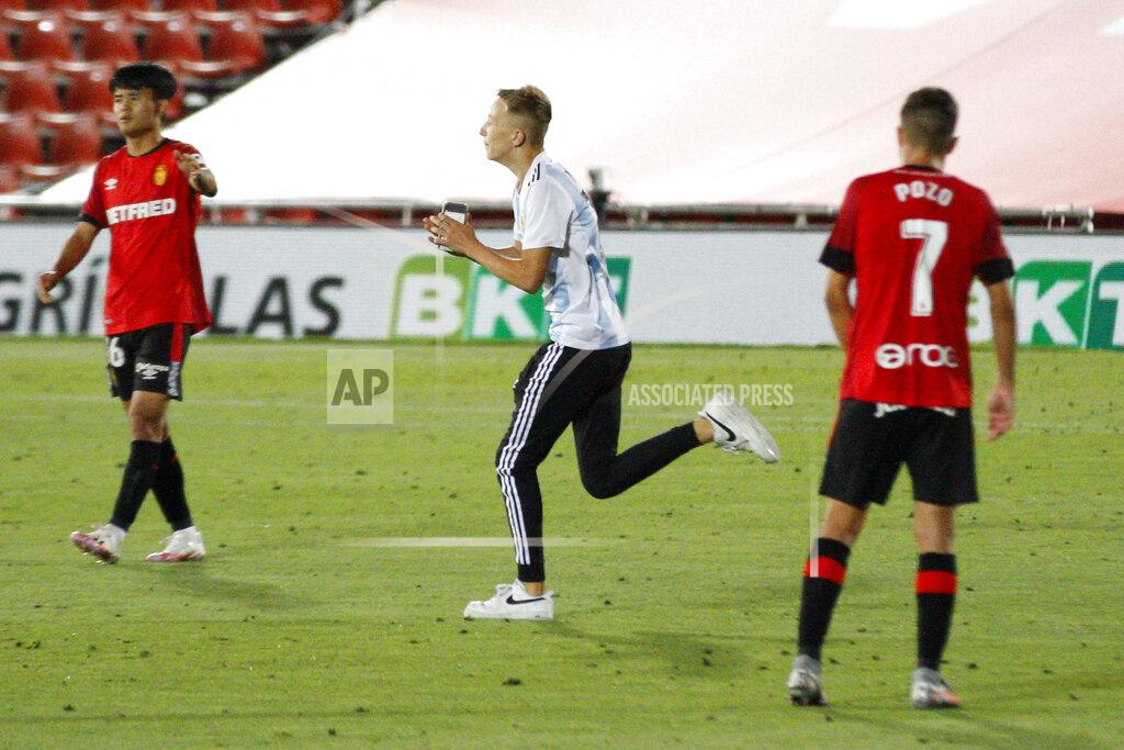 Francisco Ubilla A supporter invades the pitch, center, next to Mallorca's Kubo, left, during the Spanish La Liga soccer match between Mallorca and FC Barcelona at Son Moix Stadium in Palma de Mallorca, Spain, Saturday, June 13, 2020. With virtual crowds, daily matches and lots of testing for the coronavirus, soccer is coming back to Spain. The Spanish league resumes this week more than three months after it was suspended because of the COVID-19 pandemic. (AP Photo/Francisco Ubilla)