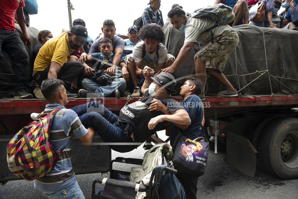 Moises Castillo Wheelchair bound migrant Wilmer Chavez, 33, is helped by fellow migrants on to the back of a freight truck that stopped to give the migrants a free ride in Rio Dulce, Guatemala, Friday, Oct. 2, 2020. A new caravan of about 2,000 migrants set out from neighboring Honduras in hopes of reaching the United States. (AP Photo/Moises Castillo)
