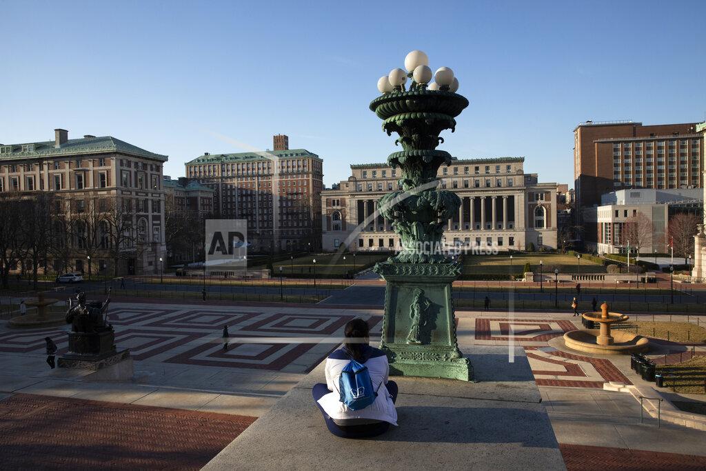 Mark Lennihan FILE - In this Monday, March 9, 2020 file photo, A woman sits on the Columbia University campus, Monday, March 9, 2020, in New York. Colleges throughout the U.S. are assuring students that this coming fall will bring a return to in-person classes, intramural sports and mostly full dormitories. But those promises come with asterisks. (AP Photo/Mark Lennihan, File)