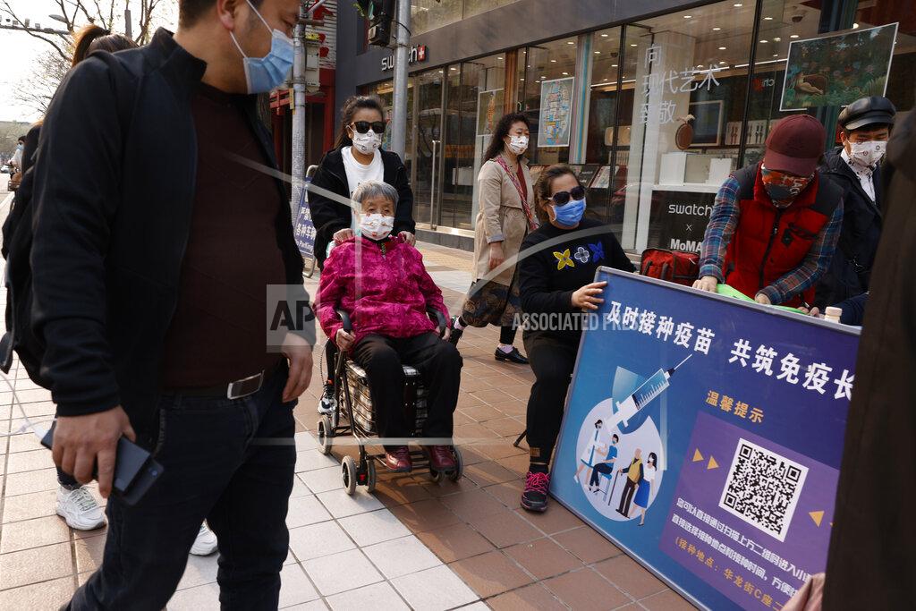 Ng Han Guan A woman in a wheel chair is pushed past a stand promoting Chinese coronavirus vaccines in Beijing Friday, April 9, 2021. In a rare admission of the weakness of Chinese coronavirus vaccines, the country's top disease control official says their effectiveness is low and the government is considering mixing them to give them a boost. (AP Photo/Ng Han Guan)