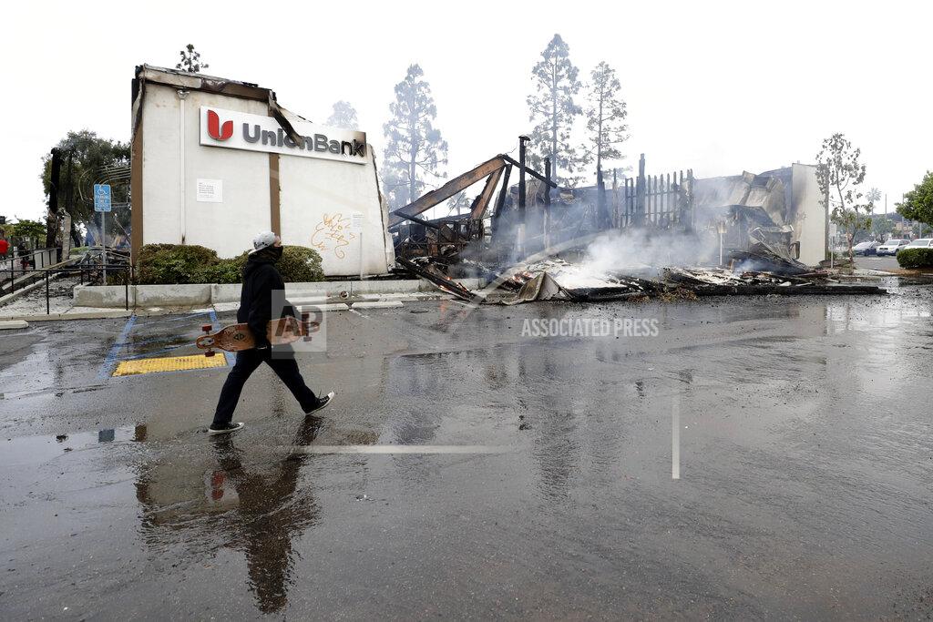 Gregory Bull A man passes a burning bank building after a protest over the death of George Floyd, Sunday, May 31, 2020, in La Mesa, Calif. Protests were held in U.S. cities over the death of Floyd, a black man who died after being restrained by Minneapolis police officers on May 25. (AP Photo/Gregory Bull)