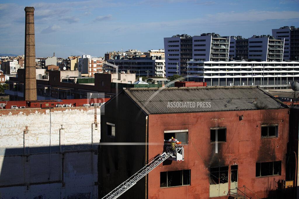 Joan Mateu Firefighters load the body of a dead person into a crane after a fire on a building in Badalona, Barcelona, Spain, Thursday, Dec. 10, 2020. Authorities in northeastern Spain say a fire has raged through an abandoned building occupied by squatters in the city of Badalona, injuring at least 17 people, including two in critical condition. Firefighters say they rescued around 30 people from windows as the building burned late Wednesday. (AP Photo/Joan Mateu)