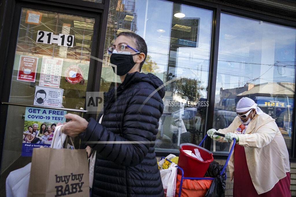 John Minchillo Pedestrians in protective masks pass a storefront on Thursday, Oct. 15, 2020, as restrictions on operations are imposed due to an increase in COVID-19 infections in the Far Rockaway neighborhood of the borough of Queens in New York. After shutdowns swept entire nations during the first surge of the coronavirus earlier this year, some countries and U.S. states are trying more targeted measures as cases rise again around the world. New York’s new round of shutdowns zeroes in on individual neighborhoods, closing schools and businesses in hot spots measuring just a few square miles. (AP Photo/John Minchillo)