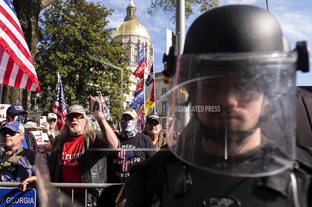 An officer in riot gear stands between supporters of President Donald Trump and counter protesters as the groups yell at each other outside of the Georgia State Capitol in Atlanta on Saturday, Nov. 21, 2020. (AP Photo/Ben Gray)