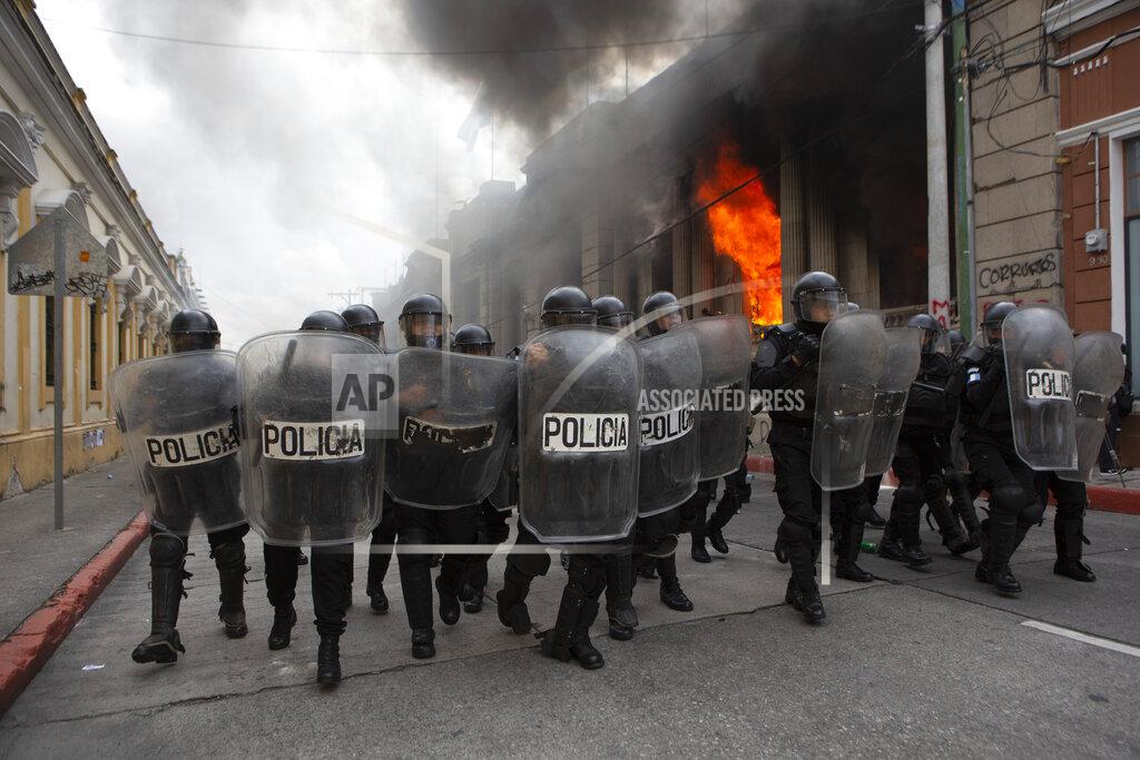 Oliver De Ros Riot police form a cordon as flames shoot out from the Congress building after protesters set a part of the building on fire, in Guatemala City, Saturday, Nov. 21, 2020. Hundreds of protesters were protesting in various parts of the country Saturday against Guatemalan President Alejandro Giammattei and members of Congress for the approval of the 2021 budget that reduced funds for education, health and the fight for human rights. (AP Photo/Oliver De Ros)