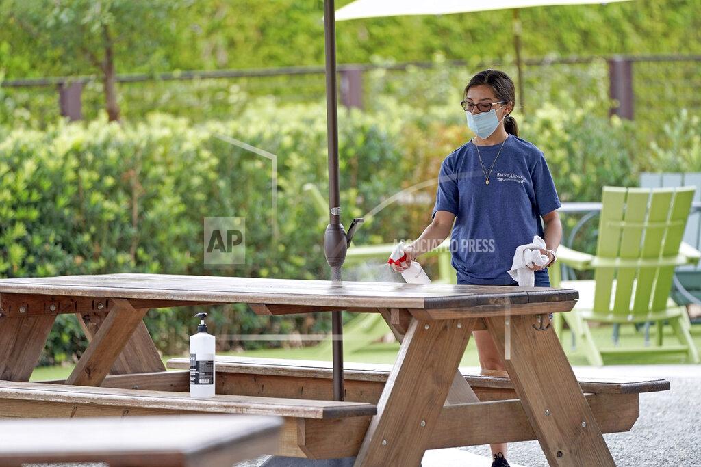 David J. Phillip Hostess Carla Alexander disinfects a table at the Saint Arnold Brewing Company, Friday, June 26, 2020, in Houston. Texas Gov. Greg Abbott announced Friday that he is shutting bars back down and scaling back restaurant capacity to 50%, in response to the increasing number of COVID-19 cases in Texas. (AP Photo/David J. Phillip)