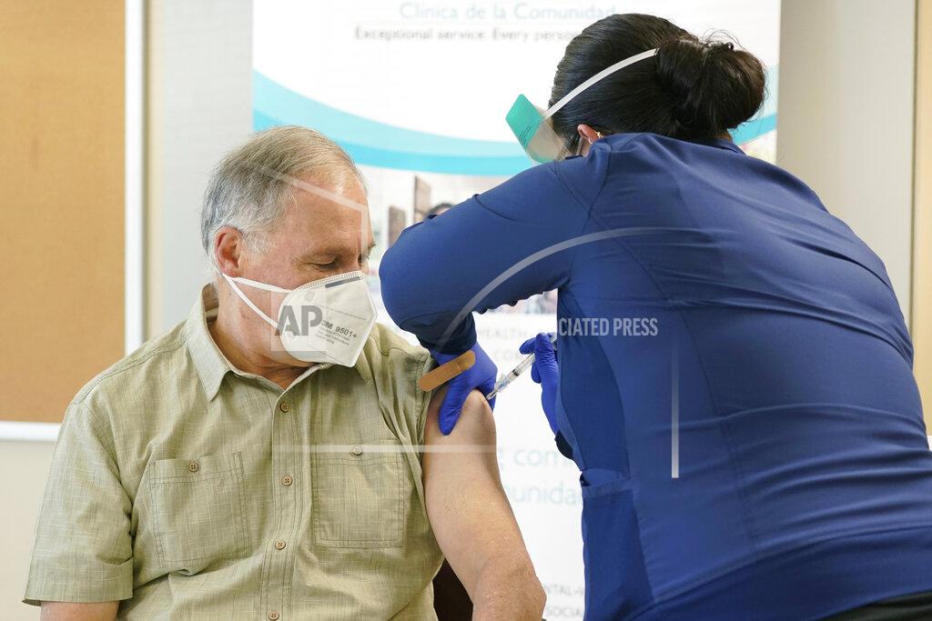 Ted S. Warren Washington Gov. Jay Inslee, left, gets the first shot of the Moderna COVID-19 vaccine, Friday, Jan. 22, 2021, from Elizabeth Smalley, right, a medical assistant at a Sea Mar Community Health Center in Olympia, Wash. Inslee's wife Trudi also received the first dose of the vaccine. (AP Photo/Ted S. Warren)
