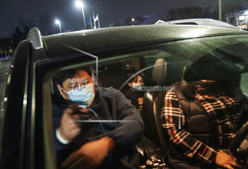 David Goldman COVID-19 patient Sall Un, 40, buckles himself in as he is picked up by his wife, Michelle Beaman, right, and his son, Bryson, 9, as he is discharged from a field hospital set up to handle a surge of COVID-19 patients Thursday, Jan. 14, 2021, in Cranston, R.I. Un arrived at Kent Hospital's emergency room where he spent three days there in isolation heavily dependent on oxygen, before recovering enough to head to the field hospital. Eight days later he was finally discharged, albeit with an oxygen tank in tow but on the lowest setting. (AP Photo/David Goldman)