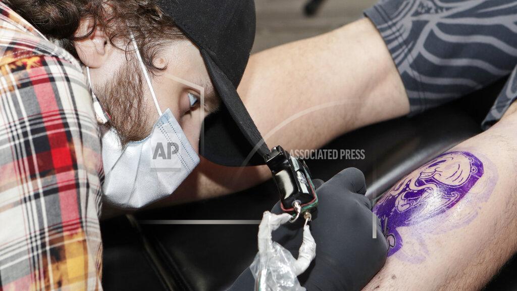 Tony Dejak Tatoo artist Kyle Jeske gives Matt Polocy a tattoo on his calf at True Art Tattoos during the coronavirus pandemic, Friday, May 15, 2020, in Cleveland. Republican Ohio Gov. Mike DeWine has said that 90% of the state's economy will be back online this weekend with Ohioans having returned to offices, factories, construction jobs and retail stores, and now outdoor eating. (AP Photo/Tony Dejak)
