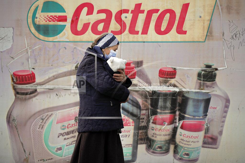Vadim Ghirda FILE- in this Wednesday, Dec. 2, 2020, file picture an elderly woman wearing a mask for protection against the COVID-19 infection carries a baby in a poor area of Bucharest, Romania. Romania will hold parliamentary elections on Sunday Dec. 6. (AP Photo/Vadim Ghirda, File)
