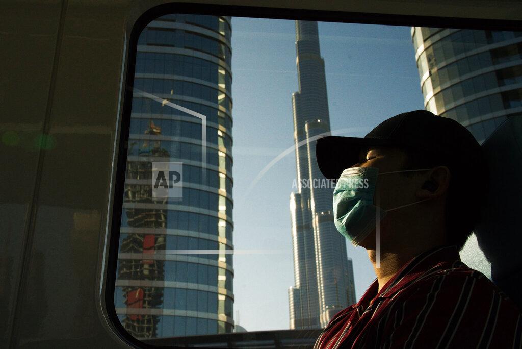FILE - In this April 26, 2020 file photo, a commuter wearing a face mask to help curb the spread of the coronavirus, sleeps aboard the driverless Metro as it passes the Burj Khalifa, the world's tallest building, in Dubai, United Arab Emirates. Travel agencies in countries across the Middle East and Africa say the United Arab Emirates has temporarily halted issuing new visas to their citizens, a so-far unexplained ban on visitors amid both the coronavirus pandemic and as the UAE normalizes ties with Israel. (AP Photo/Jon Gambrell, File)