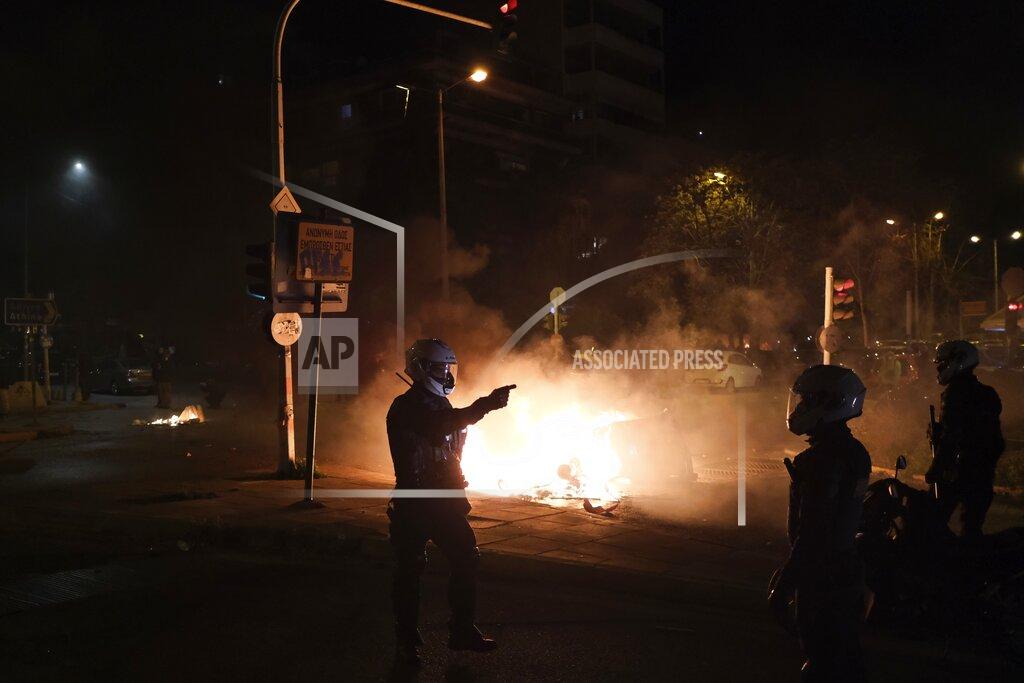 Aggelos Barai A policeman gestures as a recycle bin is on fire during clashes in Athens, Tuesday, March 9, 2021. Severe clashes broke out Tuesday in Athens after youths protesting an incident of police violence attacked a police station with petrol bombs, and severely injured one officer. (AP Photo/Aggelos Barai)