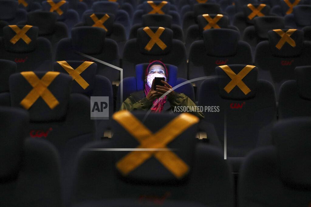Tatan Syuflana A customer uses her mobile phone before the start of a movie show as she sits amid physical distancing markers during the first day of reopening at a cinema in Jakarta, Indonesia, Thursday, Sept. 16, 2021. Cinemas in several cities shut during the deadly wave of coronavirus outbreak that hit the country in July were allowed to begin reopening with capacity limit as cases decline. (AP Photo/Tatan Syuflana)