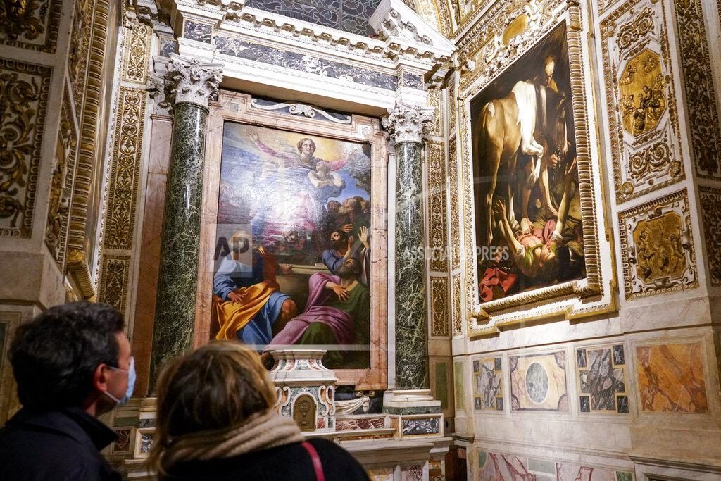 Andrew Medichini Visitors admire the "Conversion (of St. Paul) on the Way to Damascus", 1601, right, by Renaissance master Michelangelo Merisi, known as Caravaggio of 1601, flanking "The Assumption of the Virgin", 1601, by Annibale Carracci, inside the Cerasi Chapel of Santa Maria del Popolo church, Rome, Friday, Dec. 11, 2020. Like elsewhere in Europe, museums and art galleries in Italy were closed this fall to contain the spread of COVID-19, meaning art lovers must rely on virtual tours to catch a glimpse of the treasures held by famous institutions such as the Uffizi in Florence and the Vatican Museums in Rome. However, some exquisite gems of Italy's cultural heritage remain on display in real life inside the country's churches, some of which have collections of renaissance art and iconography that would be the envy of any museum. (AP Photo/Andrew Medichini)