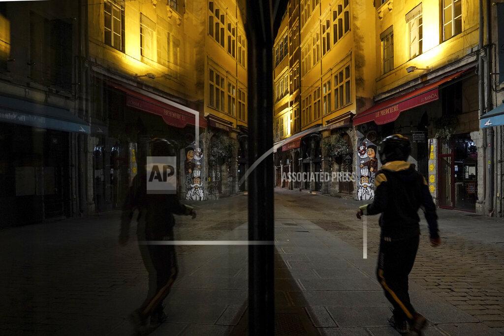 A man walks in the empty center of Lyon, central France, Saturday, Oct. 17, 2020. France is deploying 12,000 police officers to enforce a new curfew that came into effect Friday night for the next month to slow the virus spread, and will spend another 1 billion euros to help businesses hit by the new restrictions. (AP Photo/Laurent Cipriani)