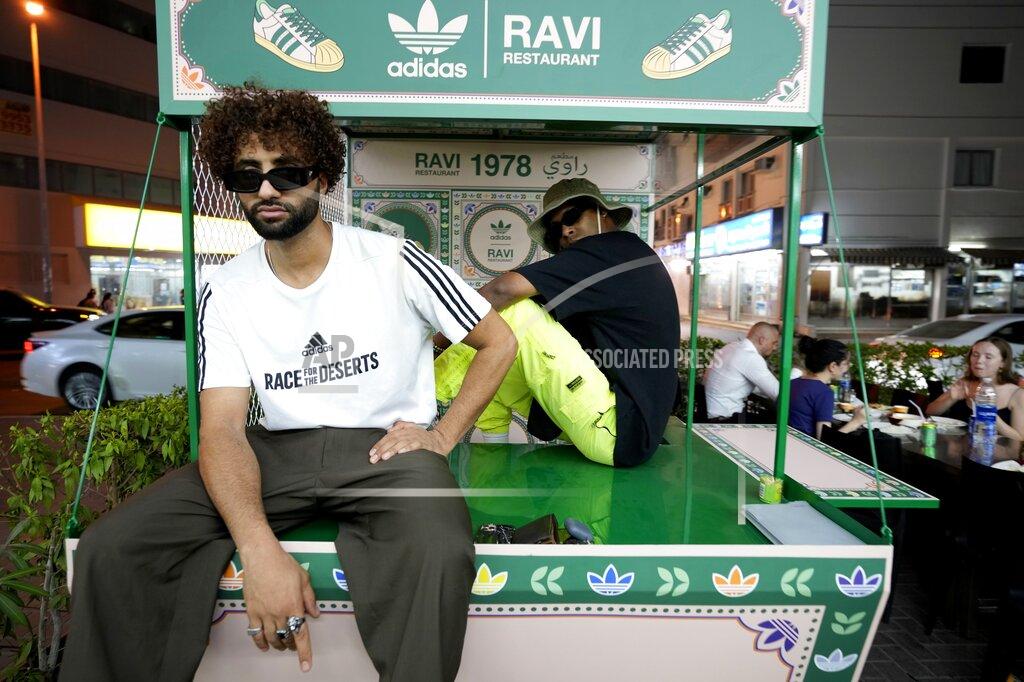 Kamran Jebreili People pose for photos with Ravi X Adidas truck in front of the Ravi restaurant in Satwa district of Dubai, United Arab Emirates, Wednesday, June 22, 2022. Adidas has teamed up with Dubai nostalgic family-owned Pakistani restaurant to release the Superstar Ravi sneaker. (AP Photo/Kamran Jebreili)