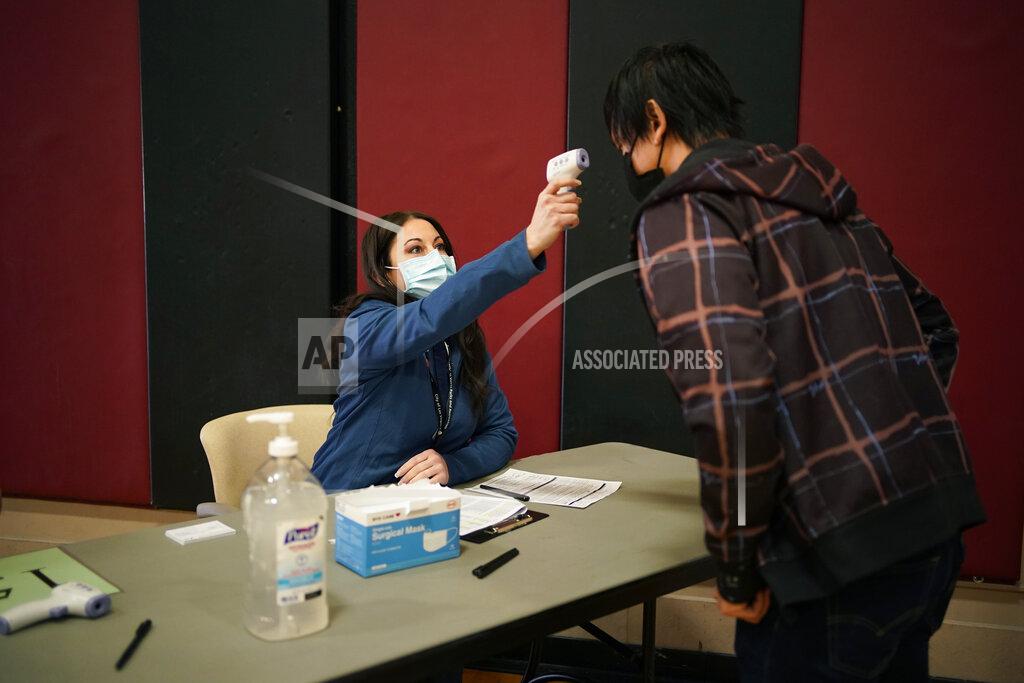 John Locher In this Feb. 17, 2021, photo, volunteer Janna Hudson takes a person's temperature while checking them in at a coronavirus vaccination site in Las Vegas. As states ramp up vaccination distribution in the fight against the coronavirus, volunteers are needed to do everything from direct traffic to check people in to keep vaccination sites running smoothly. (AP Photo/John Locher)