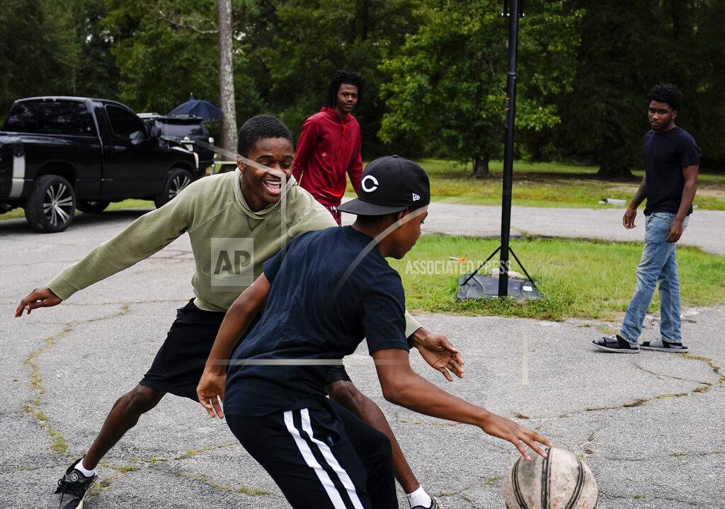 Brynn Anderson JJ Ivey, 13, center, Jay Johnson, 19, left, Te Moss, 18, back left, and Voen Ivey, 18, right, play basketball in their neighborhood in Hancock County, Saturday, Sept. 19, 2020, in Mayfield, Ga. Early on, victims of the coronavirus were mostly residents of the county's two nursing homes. Now, it's younger residents too. Coroner Adrick Ingram sees young people in town not wearing masks and gathering in big groups, and it frustrates him. ''I see people who aren't taking it seriously, maybe because they don't see what I see. They don't get to look in people's faces when they've lost somebody.'' (AP Photo/Brynn Anderson)