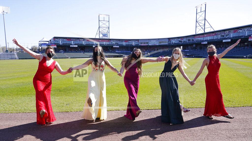 Charles Krupa While wearing their prom gowns, students pose for a photograph in the outfield at the New Hampshire Fisher Cats minor league baseball stadium in Manchester, N.H., on Monday, April 26, 2021. After a year without proms, school districts across the country are debating whether they can safely hold an event that many seniors consider a capstone to their high school experience. The nearly 300 student senior class of Manchester's Central High School are waiting to get approval from the city's board of health so they can have their prom at the outdoor venue, due to COVID-19 concerns. (AP Photo/Charles Krupa)