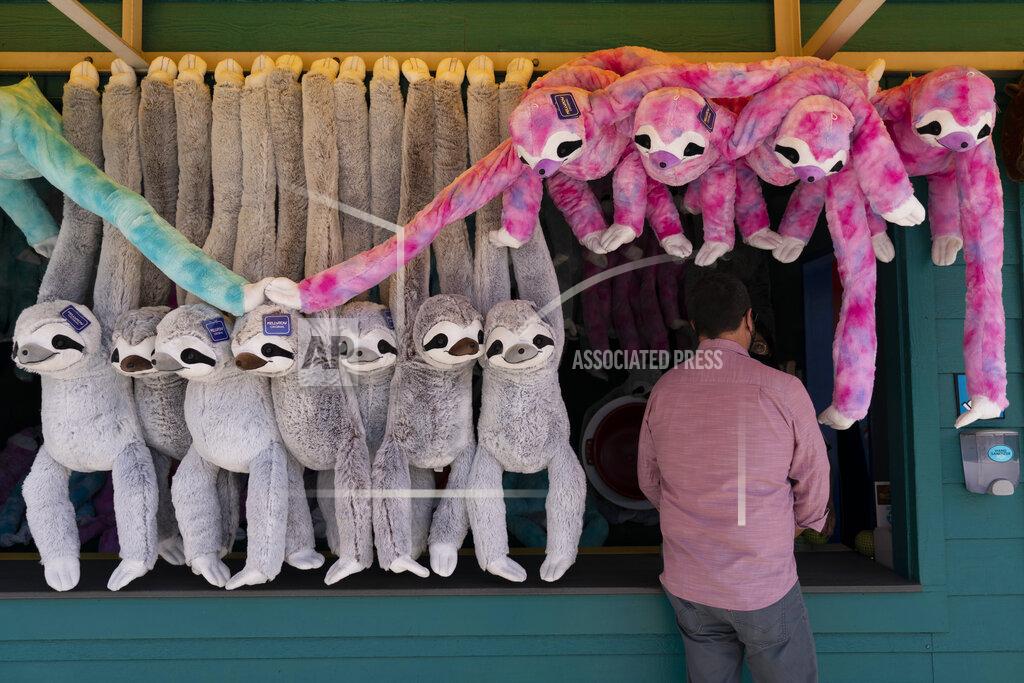 Jae C. Hong A man stands next to stuffed sloths during the Knott's Taste of Boysenberry Festival at Knott's Berry Farm in Buena Park, Calif., Tuesday, March 30, 2021. Massive Los Angeles County can reopen even more businesses, California public health officials announced Tuesday. The county of 10 million people was one of several counties, including neighboring Orange County, that moved into the state's second-least restrictive orange tier amid low coronavirus case rates and increased vaccinations. (AP Photo/Jae C. Hong)