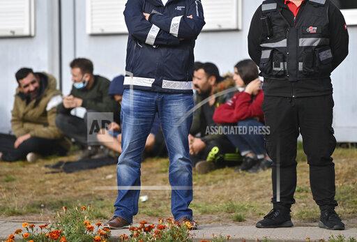 FILE-In this Oct. 6, 2021 taken photo security guards stand in front of migrants at the Central Initial Reception Facility for Asylum Seekers (ZABH) in the state of Brandenburg in Eisenhuettenstadt, Germany. German authorities say that the number of migrants arriving in the country via Poland and Belarus has gone up quickly during recent months. (Patrick Pleul/dpa via AP)