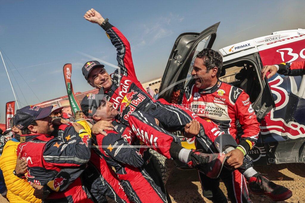Bernat Armangue Driver Carlos Sainz, of Spain, center, is lifted by Driver St»phane Peterhansel, of France, center and left, and driver Nasser Al-Attiyah, of Qatar, center and right, at the end of stage twelve of the Dakar Rally between Haradth and Qiddiya, Saudi Arabia, Friday, Jan. 17, 2020. (AP Photo/Bernat Armangue)