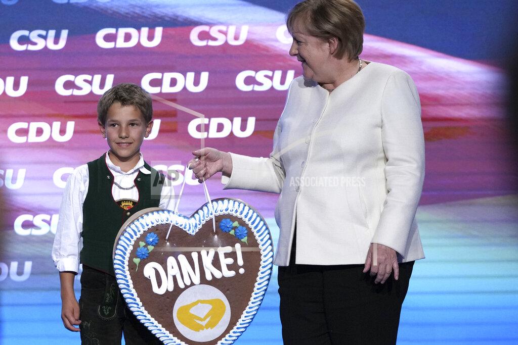 Matthias Schrader A young Bavarian boy in traditional clothes hands over a gingerbread heart reading "Thanks" to German chancellor Angela Merkel during a state election campaign in Munich, Germany, Friday, Sept. 24, 2021 two days before the General election on Sunday, Sept. 26, 2021. (AP Photo/Matthias Schrader)