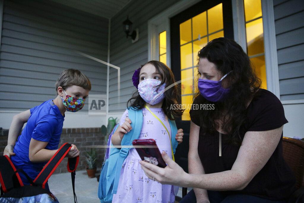 Brynn Anderson Rachel Adamus, right, shows her children, Paul, left, and Neva, 5, center, an app on her phone showing when the school bus will arrive near their home, on Monday, Aug. 3, 2020, in Dallas, Ga. The Adamus children are among tens of thousands of students in Georgia and across the nation who were set to resume in-person school Monday for the first time since March. (AP Photo/Brynn Anderson)