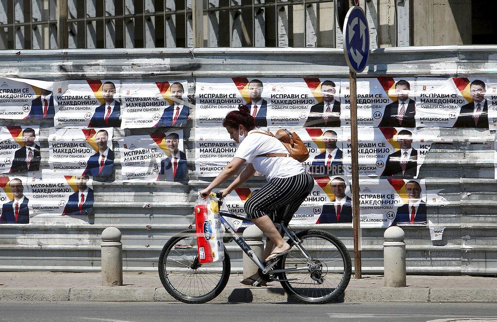 Boris Grdanoski A woman rides a bicycle past electoral campaign posters of the largest opposition party VMRO-DPMNE set on a construction fence along a street in Skopje, North Macedonia on Saturday, July 11, 2020. North Macedonia holds its first parliamentary election under its new country name this week, with voters heading to the polls during an alarming spike of coronavirus cases in the small Balkan nation. (AP Photo/Boris Grdanoski)