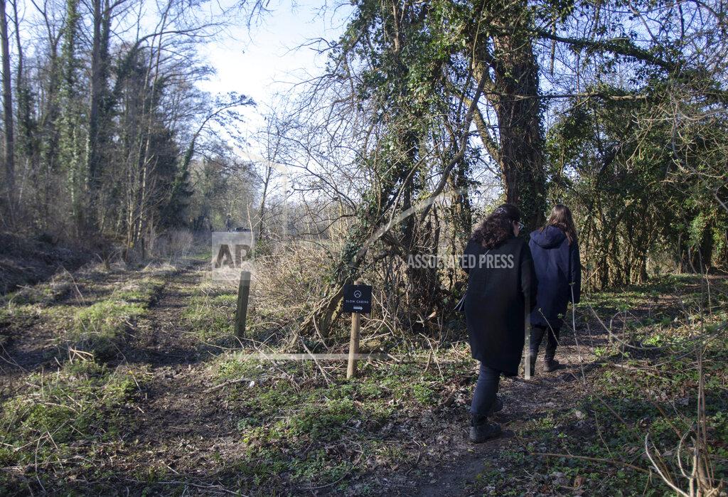 Virginia Mayo A couple follow a sign in the woods for the Slow Cabins in Zandbergen, Belgium, Sunday, Feb. 28, 2021. These Slow Cabins, set up the Belgian countryside, are the new way to vacation in pandemic times: in complete solitude and in the middle of nowhere. The wooden cabins are fully sustainable, provided you don't stay in the shower too long and you can live without Wi-Fi (AP Photo/Virginia Mayo)