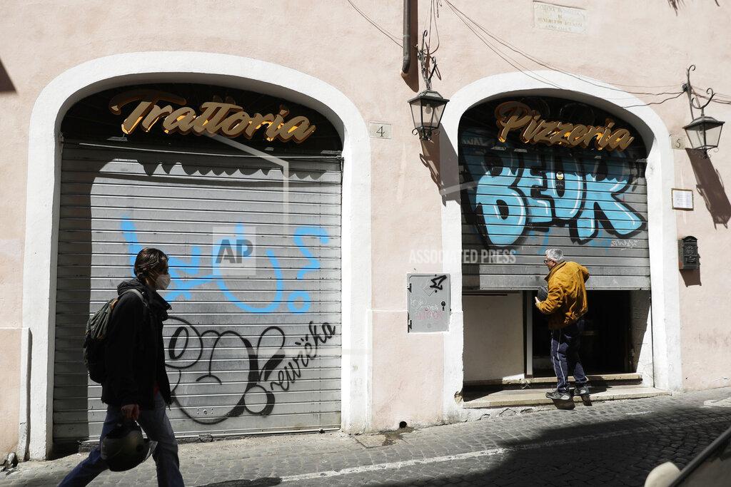 Gregorio Borgia A man opens the shutter of a Restaurant in Rome, Friday, April 9, 2021. Italy has seen a stabilizing of the new variant-fueled infections over the past three weeks, though its daily death count remains stubbornly high, averaging between 300-500 COVID-19 victims per day, and its ICU capacity for virus patients is well over the threshold set by the government. (AP Photo/Gregorio Borgia)