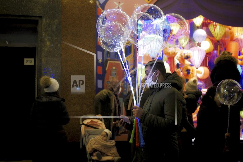Thibault Camus A man holds light balloons as he checks his phone on a sidewalk next to a department store in Paris, Thursday, Dec. 31, 2020. (AP Photo/Thibault Camus)