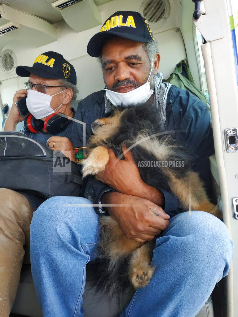 In this photo released by Colombia's Army Press Office, Daniel Max Guggenhein from Switzerland, left, and Jose Ivan Alburneque Matias from Brazil, right, sit in a helicopter after being rescued by Colombia's Army in Popayan, Colombia, Thursday, June 18, 2020. Both foreigners were kidnapped 3 months ago by dissents members of the Revolutionary Armed Forces of Colombia. Matias is holding his pet dog that was kidnapped along with his owner and accompanied him through the whole ordeal. (AP Photo/Colombia's Army Press Office)
