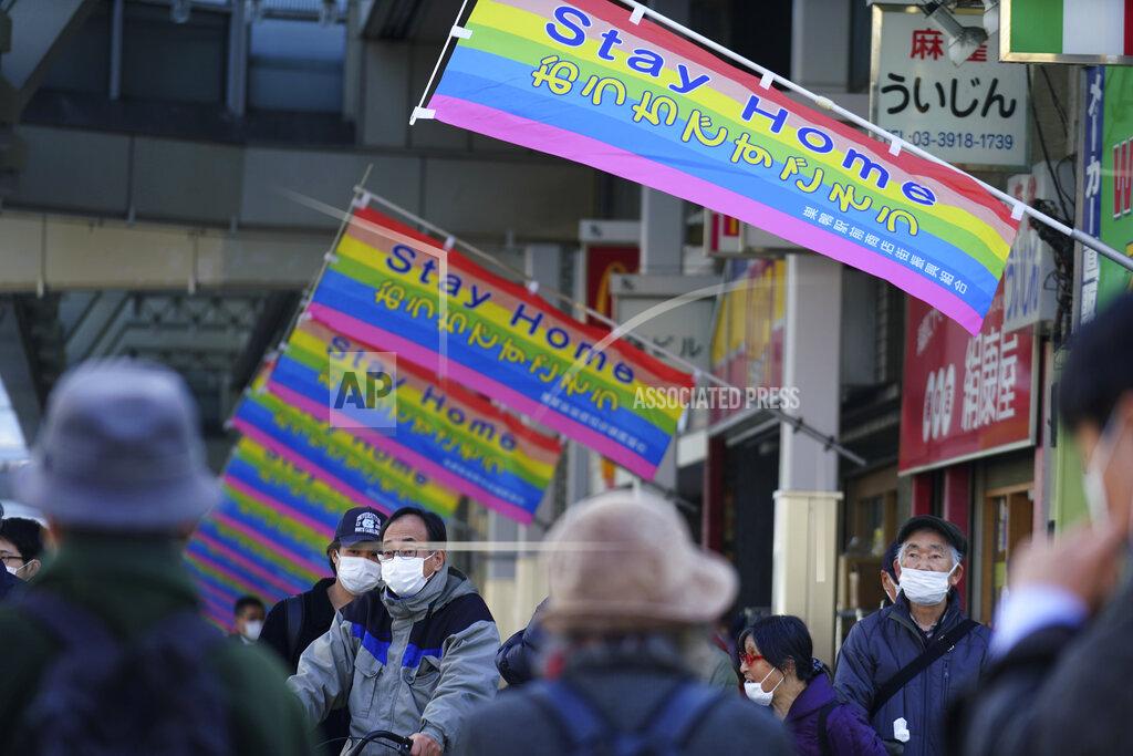 Eugene Hoshiko People wearing protective masks to help curb the spread of the coronavirus wait for a traffic light near banners reading " Stay Home" hoisted along a shopping street in Tokyo Thursday, Jan. 14, 2021. The Japanese capital confirmed more than 1500 new coronavirus cases on Thursday. (AP Photo/Eugene Hoshiko)
