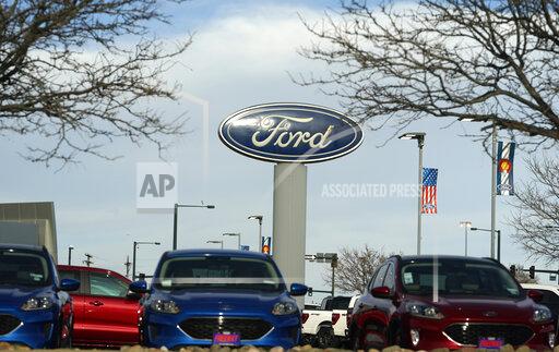 In this Sunday, April 25, 2021, photograph, the blue oval logo of Ford Motor Company is shown over a row of unsold 2021 Escapes at a dealership in east Denver. The global computer chip shortage cut into third-quarter profits at both Ford and crosstown rival General Motors, with both companies having to temporarily close factories, pinching supplies on dealer lots, according to results announced Wednesday, Oct. 27. (AP Photo/David Zalubowski)
