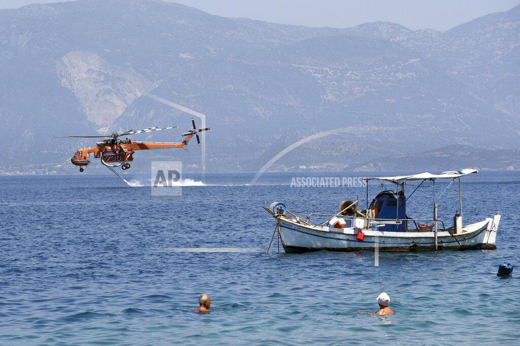 Andreas Alexopoulos A helicopter fills up with water from the sea near Ziria village, east of Patras, Greece, Sunday, Aug. 1, 2021. A wildfire that broke out Saturday in western Greece forced the evacuation of four villages and people on a beach by the Fire Service, the Coast Guard and private boats, authorities said. (AP Photo/Andreas Alexopoulos)
