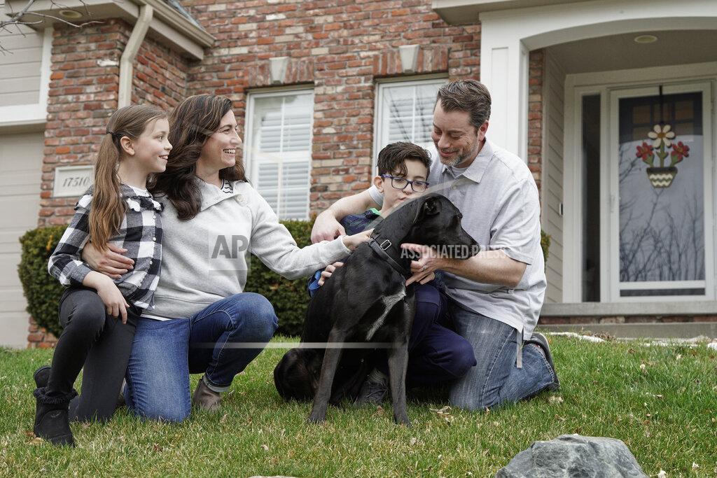 In this March 27, 2020, photo, Kim Simeon; her husband, Adam; and children, Annabel, 9, and Brennan, 11, pose for a photo with Nala, a dog they are fostering, in Omaha, Neb. The Simeon family was headed home to Omaha from a much-needed Smoky Mountains vacation when Kim Simeon spotted a social media post from the Nebraska Humane Society, pleading with people to consider fostering a pet. (AP Photo/Nati Harnik)
