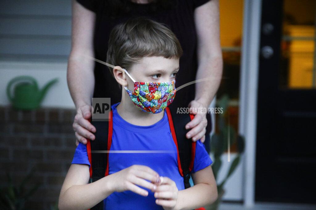 Brynn Anderson Rachel Adamus holds her son Paul, 7, on their porch before the bus arrives for the first day of school on Monday, Aug. 3, 2020, in Dallas, Ga. Adamus is among tens of thousands of students in Georgia and across the nation who were set to resume in-person school Monday for the first time since March. (AP Photo/Brynn Anderson)