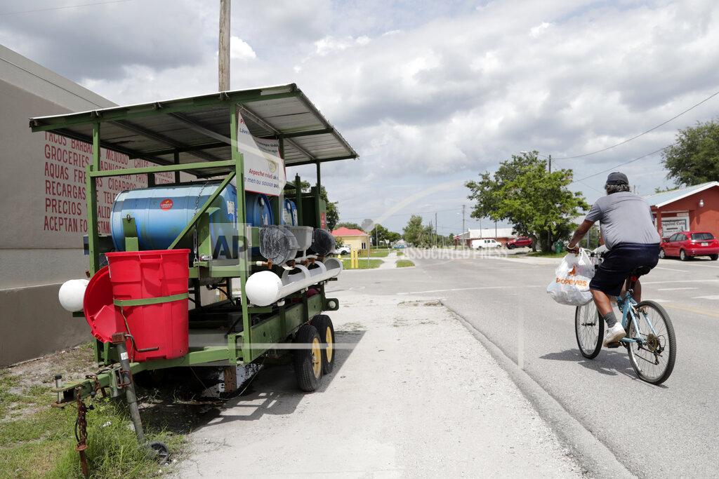 Lynne Sladky In this Monday, June 8, 2020, photo, a man cycles past a hand washing station set up outside of a popular supermarket amid the new coronavirus pandemic in Immokalee, Fla. Even as the pace of new cases has moderated in the state of Florida, this poor farmworking town in rural Florida is in the throes of an outbreak. (AP Photo/Lynne Sladky)