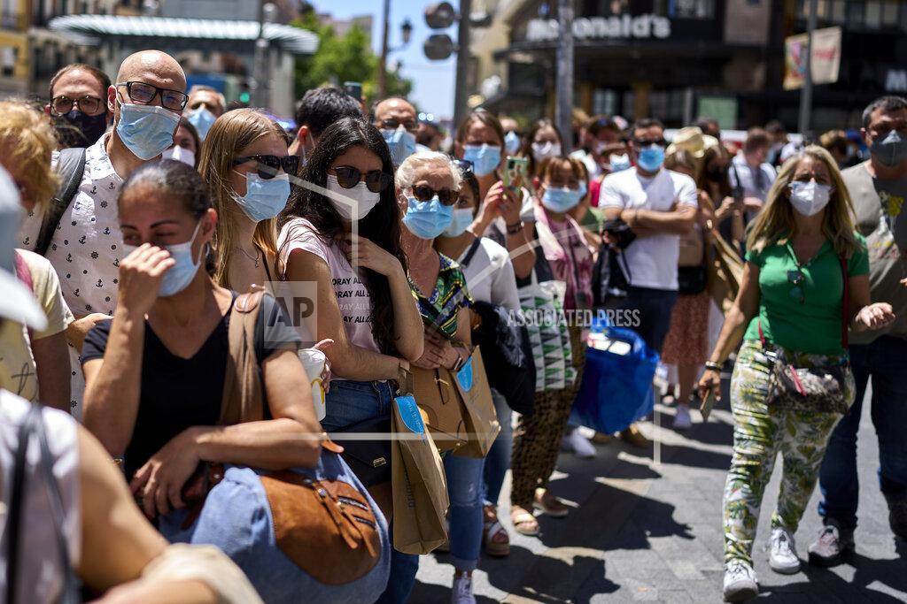 Manu Fernandez People wearing face masks stand along a street in Madrid, Spain, Thursday, June 24, 2021. Spain is easing its COVID-19 pandemic rules, permitting people to stop wearing masks outdoors and allowing sports fans back into stadiums. Almost a year after face masks became mandatory indoors and outdoors, people from Saturday will no longer be required to wear them outside as long as they can stay at least 1.5 meters (5 feet) apart. (AP Photo/Manu Fernandez)