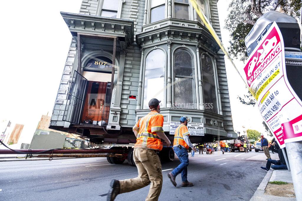 Noah Berger Workers pass a Victorian home as a truck pulls it through San Francisco on Sunday, Feb. 21, 2021. The house, built in 1882, was moved to a new location about six blocks away to make room for a condominium development. According to the consultant overseeing the project, the move cost approximately $200,000 and involved removing street lights, parking meters, and utility lines. (AP Photo/Noah Berger)