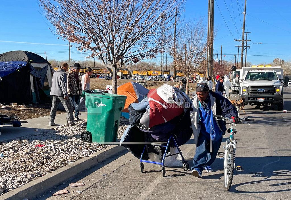 Tim Vandenack Residents of a tent city encampment on 33rd Street in Ogden, Utah move their belongings from the side of the street on Tuesday, Dec. 1, 2020, to make way for Ogden City clean-up crews, wearing white in the background. (Tim Vandenack/Standard-Examiner via AP)
