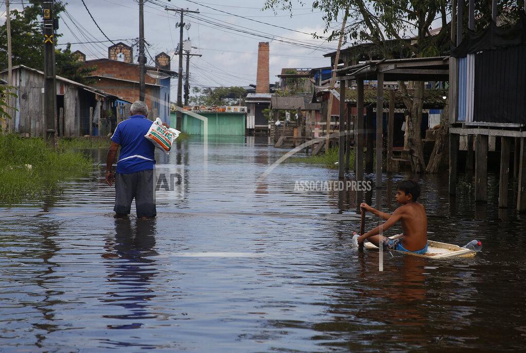 Edmar Barros A boy uses a fridge door to float across a street flooded by the rise of the Negro river in Iranduba, Amazonas state, Brazil, Monday, May 23, 2022. The Amazon region is being hit hard by flooding with 35 municipalities that are facing one of their worst floods in years and the water level is expected to rise over the coming months. (AP Photo/Edmar Barros)