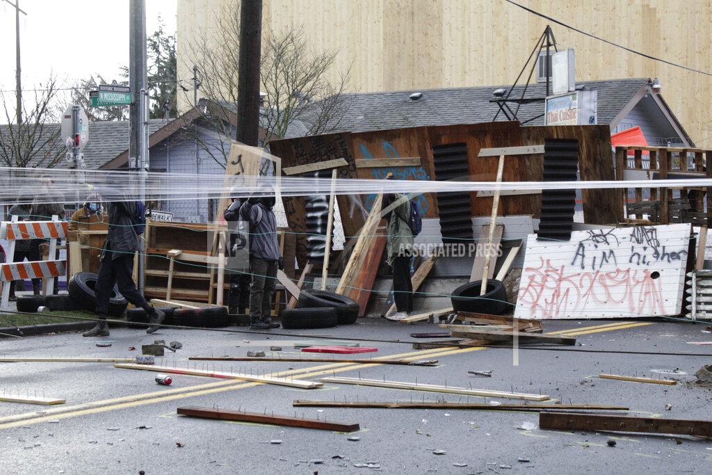 Protesters stand behind barricades at their encampment outside a home in Portland, Ore., on Wednesday, Dec. 9, 2020. Makeshift barricades erected by protesters are still up in Oregon's largest city a day after Portland police arrested about a dozen people in a clash over gentrification and the eviction of a family from a home. (AP Photo/Gillian Flaccus)