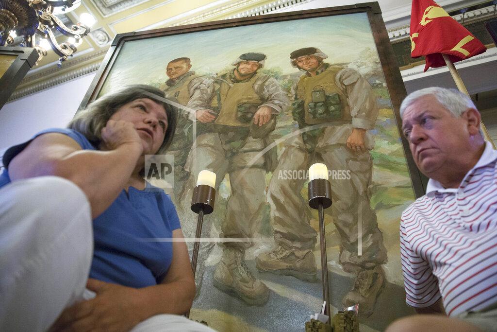 John Minchillo FILE—In this file photo from July 28, 2015, Pat Murray, left, and Ken Kreuter sit beneath a portrait of their son Marine Sgt. David Kreuter, top right, at the traveling Eyes of Freedom Lima Company Memorial then displayed at the Cincinnati Masonic Center. Kreuter was one of 14 Marines from Ohio-based Lima Company who were killed by an IED explosion in Iraq 15 years ago. Some survivors and families of those killed had planned a 15-year reunion this weekend, but it had to be canceled amid restrictions for the COVID-19 pandemic. (AP Photo/John Minchillo, File)