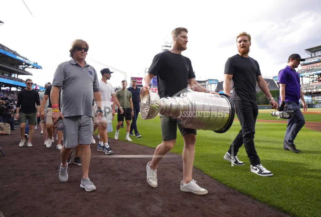 David Zalubowski Colorado Avalanche captain Gabriel Landeskog, second from right, walks next to Nathan MacKinnon, who carries the Stanley Cup as the NHL hockey team is honored by the Colorado Rockies before the baseball team's game against the Los Angeles Dodgers on Wednesday, June 29, 2022, in Denver. (AP Photo/David Zalubowski)