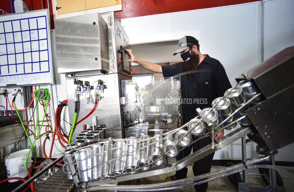 Kristopher Radder Connor Busch, the head brewer at Whetstone Craft Beers, in Brattleboro, Vt., keeps an eye on a new machine that is filling up cans with their Updog Stout on Friday, Aug. 28, 2020. The new canning line was installed sooner than planned because the COVID-19 pandemic forced businesses to change their business model. (Kristopher Radder/The Brattleboro Reformer via AP)
